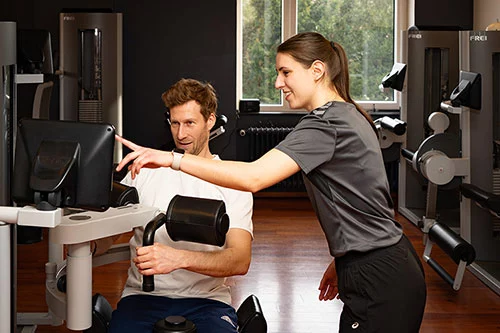 Personal trainer guides a client using a cable weight machine in a gym, pointing at the screen or monitor